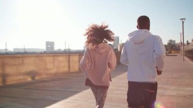 İki etnik çeşitlilikte arkadaşın şehir merkezinde gündüz vakti kaldırımda koşarken orta açıdan çekilmiş bir fotoğrafı.