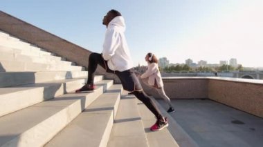 Genç, etnik çeşitlilikte bir çiftin sabah merdivenlerde bacak esnetme egzersizleri yaptığı bir sahne.