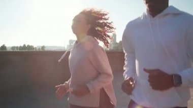 Kafkasyalı bir kadınla birlikte şafak vakti kaldırımda koşu yapan Afrikalı Afrikalı bir adamın yavaş çekim görüntüleri.