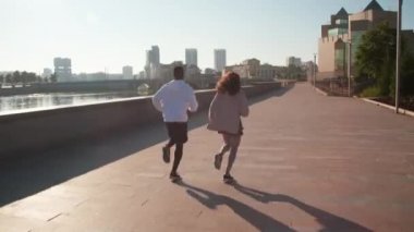 Arka planda, güneşli bir günde arka planda güzel şehir manzarasıyla birlikte koşan atletik çiftin tam görüntüsü.