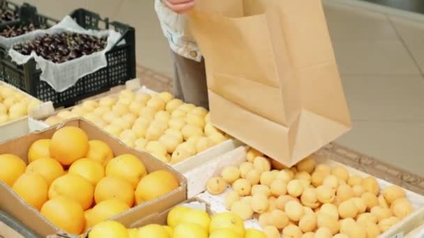 市場の果物スタンドから新鮮なオレンジを拾うと紙の袋にそれらを入れて認識できない若い男のハンドヘルドショット — ストック動画