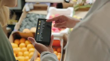 Bir çiftin cep telefonundan alışveriş listesine bakarken ve pazardaki meyve standında dikilirken sohbet ederken çekilmiş omuz fotoğrafını izliyorum.