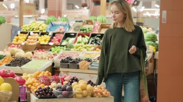 屋内市場を歩いて新鮮な食材を見て若い女性の手持ち中出し 彼女は果物のスタンドでベリーの匂いを嗅いで歩いている — ストック動画
