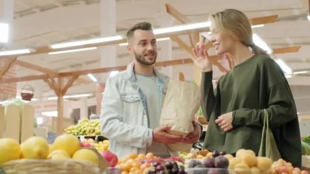 市場で果物スタンドに立っている若い女性と男の低角度中出しや新製品のための買い物中に熟した桃の香り — ストック動画