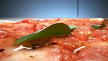 Ekstra saf zeytinyağını pepperonili, peynirli ve taze domatesli pizza tepesine serpiştiriyorum.
