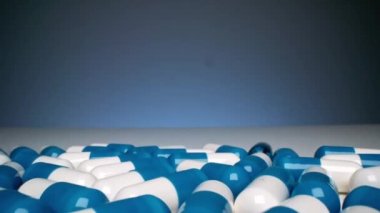 Stüdyodaki açık beyaz masaya dökülen bir sürü beyaz ve mavi kapsül uyuşturucu hapının makro görüntülerini dağıtıyorum.