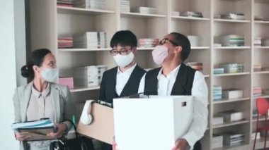 Koruyucu maskeler takan üç neşeli çok ırklı insan, çalışmalarından sonra eşyalarını kutuya koyup birbirleriyle konuşuyorlar.