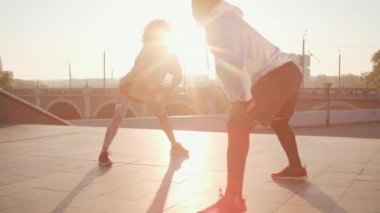 Kafkasyalı kadın ve Afro-Amerikan erkek spor giyim kuşağı giymiş çift antreman yaparken şafakta yan yana hamleler yaparken.