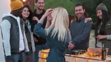 Çok ırklı arkadaşlarıyla dans eden, gülen ve DJ 'lik yapan, enerjik disko müziği çalan çekici beyaz bir kadının orta boy yakın çekimi.