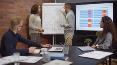 İki çok ırklı iş ortağının modern açık uzay ofisinde iş arkadaşlarının önünde el sıkışırken ve gülümserken orta derecede görüntüsü.