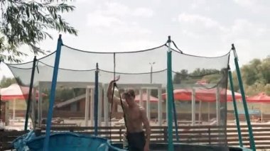 Tam bir atletik çocuk. Açık havada trambolinde zıplıyor. Ön, arka ve yan taklalar atıyor.