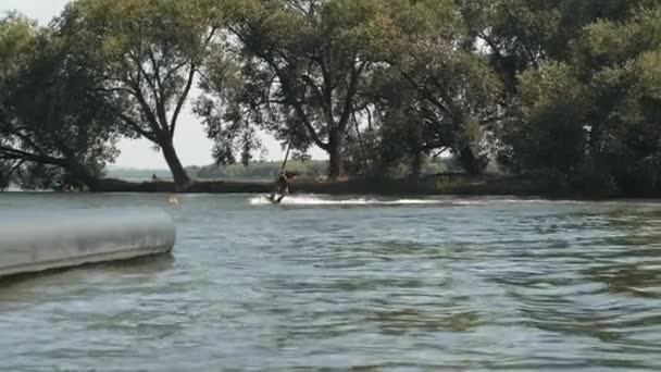 浮力ベストとヘルメットウェイクボードで若い男のフルショット湖で日光浴で水にスライド — ストック動画
