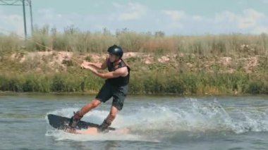 Su sporu kıyafetleri giymiş atletik bir çocuğun, su sıçratan suyla gölde kayarken görüntülerini izliyoruz.