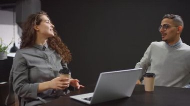 Orta doğulu ofis çalışanının modern çatı katında bilgisayarında çalışan meslektaşına kahve getirirken çekilmiş resmi.