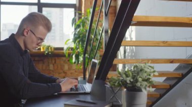 Çok ırklı iş arkadaşları pencerenin kenarında parlak modern ofis tarzında konuşurken konsantre olmuş erkek ofis çalışanlarının bilgisayarda daktilo kullanışının yan görüntüsü.