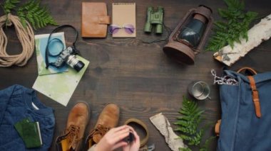 Pusula açıp ok atan, tanınmayan bir kadının düz açılı görüntüsü. Tahta masanın üzerinde huş ağacı kütükleri ve eğreltiotu ile süslenmiş seyahat aksesuarları.