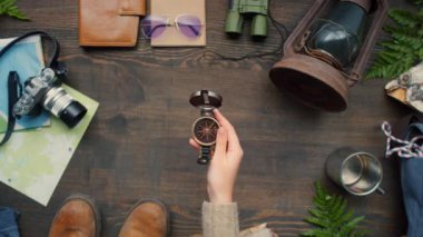 Tahta masanın üzerinde pusula tutan tanınmayan bir kadının en üst görüntüsü, sonra da bırakıyor. Seyahat aksesuarları masada yatıyor.