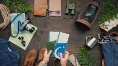 Pasaportları ve uçak biletlerini üzerinde seyahat aksesuarları olan ahşap masaya koyan tanınmamış bir kadının fotoğrafının hemen üstünde.