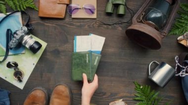 Üst manzara tanınmayan bir kadının üzerine çeşitli seyahat aksesuarları ve ahşap masaya pasaport ve bilet koyması.