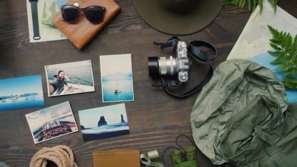 木製のテーブルの上に横たわる最近の旅行からの旅行用品 カメラ ランタン シダと写真のPanトップビュー — ストック動画