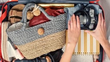 Tanınmayan bir kadının fotoğraf makinesini ve gerekli şeyleri bavula koyup sonra da kapağın üstüne pasaport ve uçak biletlerini koyması.