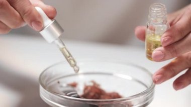 Tanınmayan kadın ellerine yakın çekim. Cam kasedeki ev yapımı temizlik malzemelerine sarı gerekli yağ damlaları ekliyor. Her şeyi çatalla karıştırıyor.