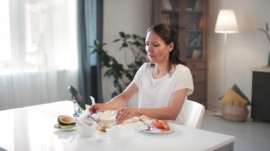 40 'lı yaşların ortasında gülümseyen çekici bir kadının havuç, avokado, yumurta ve fırçayla yapılmış yaşlanma karşıtı maske taktığı orta boy bir fotoğraf.