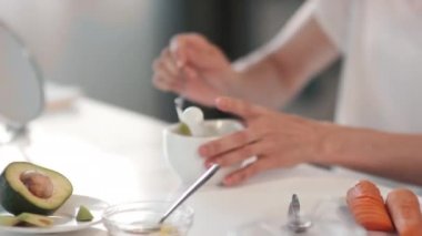 Avokadoyu kabın içine boşaltıp, ev yapımı yüz maskesi için pürüzsüz macuna batıran, yaşlanmayı önleyici etkiye sahip tanınmamış kadın ellerinin yakın çekimi.