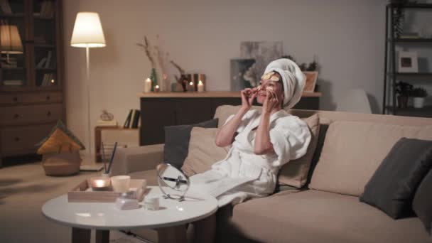 お風呂の後に陽気な中年女性のフルショット自宅で暖かい夜にリラックスバナナスライスとソファの上に横たわる若返りとさわやかな効果のための顔 — ストック動画