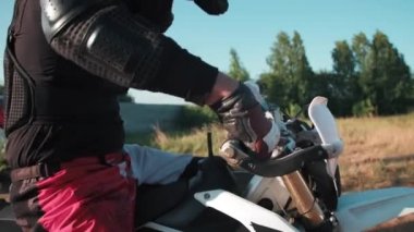 Motosiklet üzerinde tam teçhizatlı bir adamın kickstand 'ı çekerken, sonra motoru döndürüp uzaklaşırken görüntüsü.