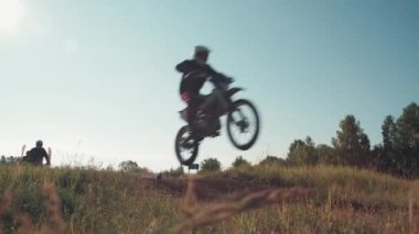 Düşük açılı, vitesli, kasklı motosikletli, off-road pistinde motosiklet süren ve zıplayan orta açı.