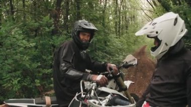 Kask takan neşeli motosikletli erkek motosikletlilerin yemyeşil ormanlarda birbirlerine beşlik çakışlarını el kamerasıyla izliyorlar.