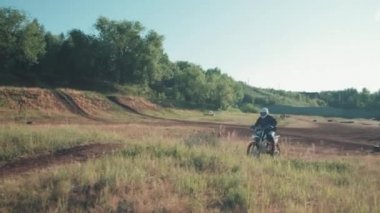 Güneşli bir günde off-road pistinde kaskla motosiklet süren bir adamın görüntüsü.