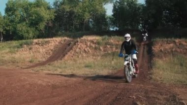 Takımlı ve kasklı adamların off-road pistinde motosiklet sürerken görüntülerini izliyoruz.