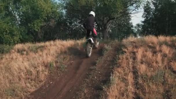 オフロードトラック上の上り坂のオートバイに乗るギアやヘルメットの男性の追跡 — ストック動画