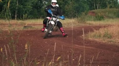 Kasklı, teçhizatlı, motosiklet süren ve ormandaki off-road pistinden dönen adamların yavaş çekimleri.