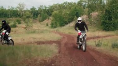 Ormandaki toprak yolda motosiklet süren ve birbiriyle yarışan, vites ve kask takan insanların izini sürmek.
