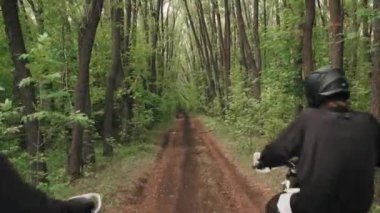 Ormanda yemyeşil yollarda motosiklet süren kasklı ve teçhizatlı adamların görüntülerini izliyoruz.