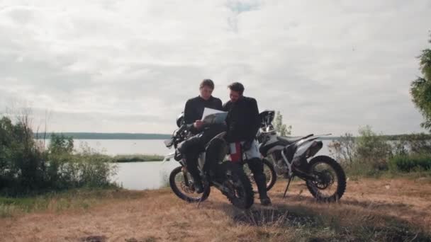在阴郁的日子里追踪坐在湖边休息的年轻男性骑摩托车者的车速 并查看地图 — 图库视频影像