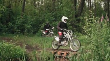 Ormanda motosiklet süren ve küçük tahta köprüden geçen, teçhizatlı ve kasklı adamların izini sürüyorum.