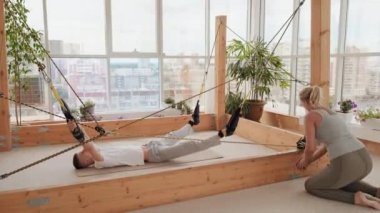 Genç bir kadının dönme mekanizmasını çevirmesi ve partnerinin eklemleri ve bağları güçlendirmek için kullanılan özel esneme simülatörünü kaldırması.