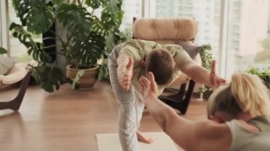 Genç erkek Yogi 'nin, kadınlara esneme egzersizleri öğretirken, spor salonunda, panoramik pencerelerle öne eğildiğini gösteren bir fotoğraf.