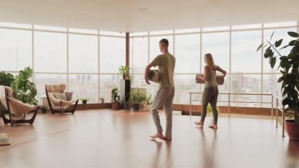在明亮宽敞的瑜伽演播室里 身穿运动服的年轻夫妇在地板上翻滚着瑜伽垫 全景全景尽收眼底 城市景色宜人 — 图库视频影像