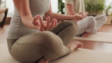 Tanımlanamayan erkek ve kadının, stüdyoda panoramik pencereli özel parmak pozları kullanarak çift yoga eğitimi almalarının orta kesiminde.