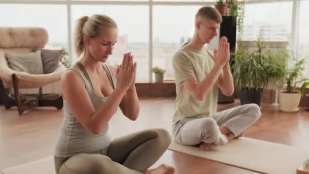 情侣们一起练习瑜伽的全景 双手合十 双目紧闭 坐在地上的瑜伽垫上 — 图库视频影像