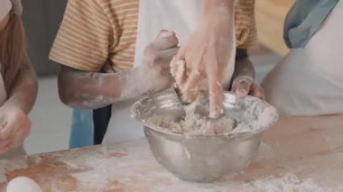 Metalik kasede hamur yoğuran, masada büyük kaşığı olan, önlüklü arkadaşlarının tanımadığı öğrencilerin elleri.