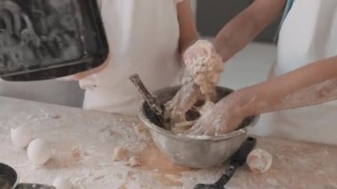 Tanınamayan küçük insanların hamur yaptığı yüksek açı, elleriyle yoğurmak, metal kaseye un eklemek. Önlük takan çocuklar, masanın yanında oturuyorlar.