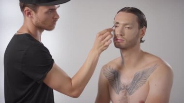 Erkek modellerin kaşlarını taramak için spoolie fırçası kullanan profesyonel erkek makyaj sanatçısının orta boy fotoğrafı.