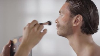 Orta boy, tanınmayan profesyonel MUA fırça ve bronzlaştırıcı kullanan erkek müşterinin alnına ve elmacık kemiklerine...