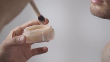 Tanımlanamayan makyaj sanatçıları tarafından yavaş yavaş takip ediliyor fırçaya toz yapıştırılıyor ve erkek modelin yüzüne uygulanıyor.